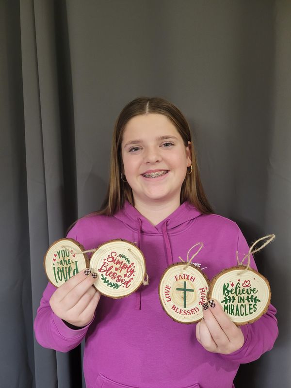 Jocey holding four hand-painted wood-slice ornaments she crafted for her Benjamin Project
