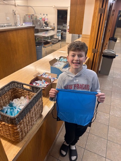 Max holds a New Prague drawstring bag next to a basket of hygiene kit supplies