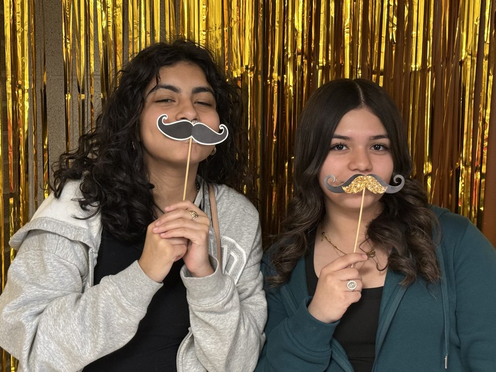 Two students holding mustache props at the photo booth fundraiser