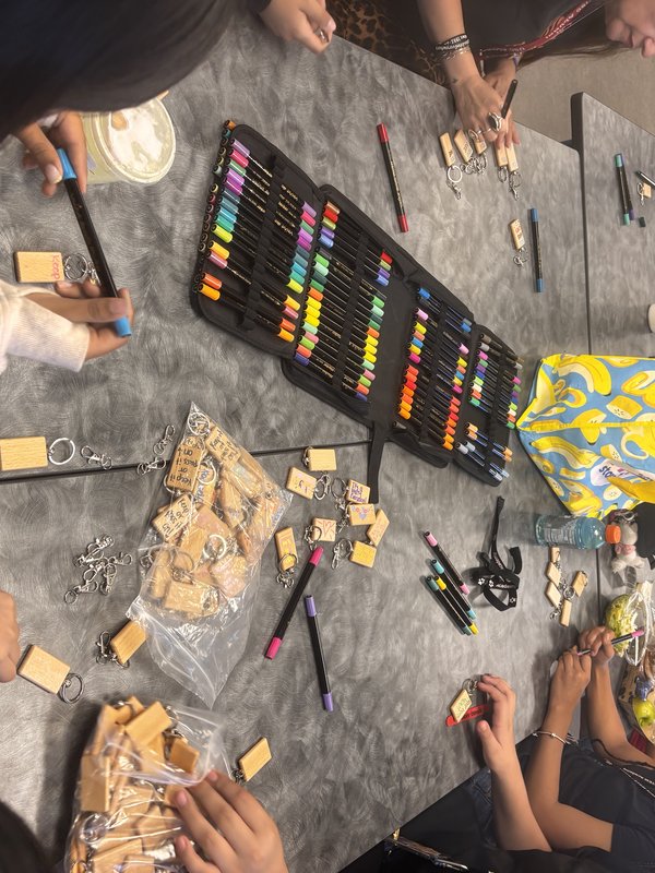 Paint markers, keychain hardware, and bags of finished wooden keychains spread across the crafting table