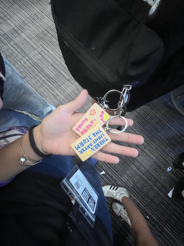 A hand holding two finished keychains with uplifting hand-lettered messages