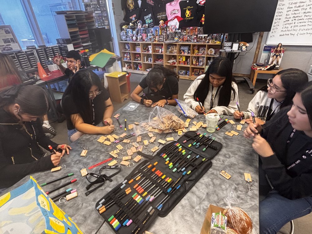 Anevay and classmates decorating wooden keychains with paint markers around a classroom table