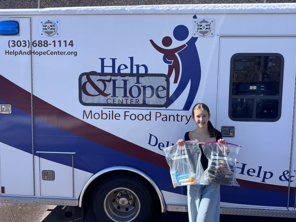 A student holding two clear bags of hygiene supplies in front of the Help & Hope Center mobile food pantry van