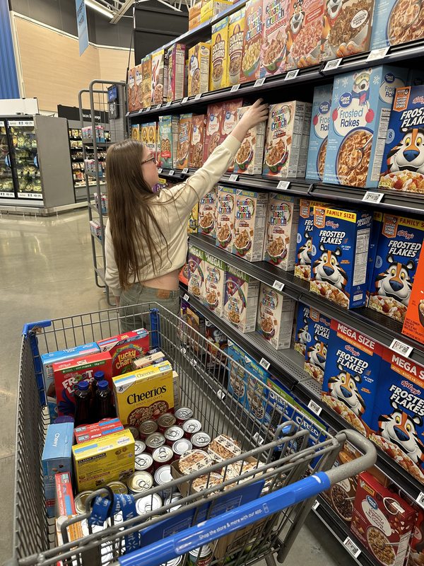 McKenzie reaching for a box of cereal on a store shelf while filling her donation cart