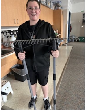 A student holding a new rake used to prepare the greenhouse's native seed garden