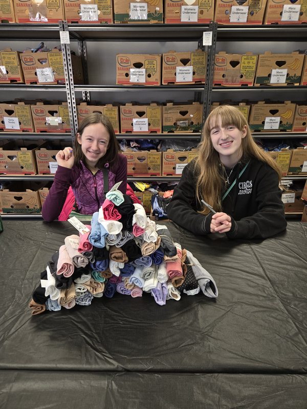 Two students smiling behind a large pyramid of the 61 bundled pairs they prepared for The Drawer