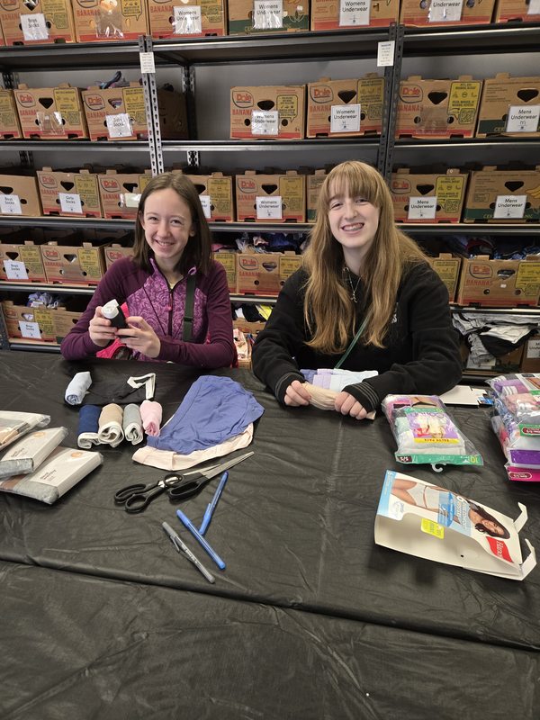 Two students sorting and bundling packages of new underwear at a donation center table