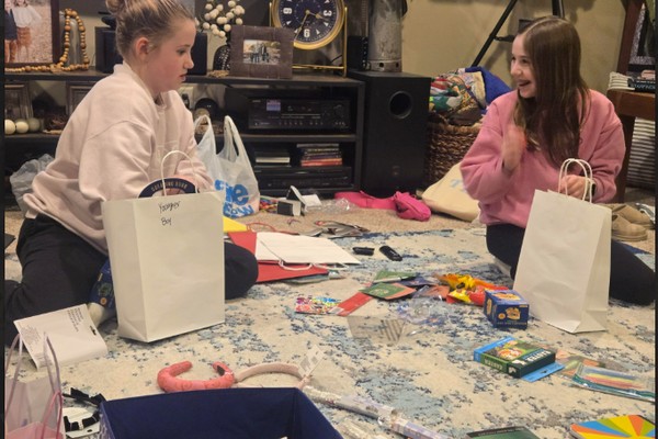 Two students sitting on the floor sorting toys and books into gift bags