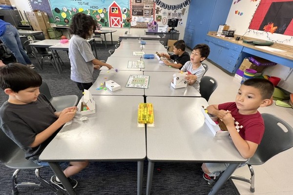 Elementary students seated at desks opening white sensory-kit boxes in a decorated classroom