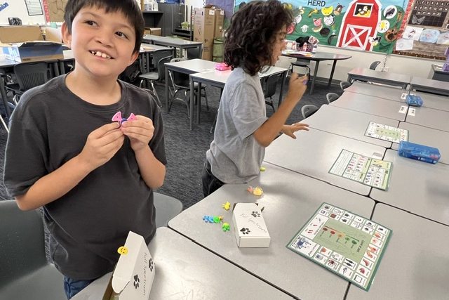 A smiling young student holding up a small pink fidget toy in a classroom