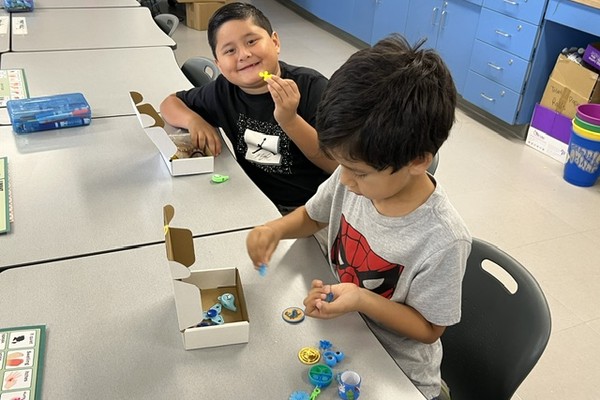 Two young students at a classroom table exploring small sensory fidget toys from an open kit box